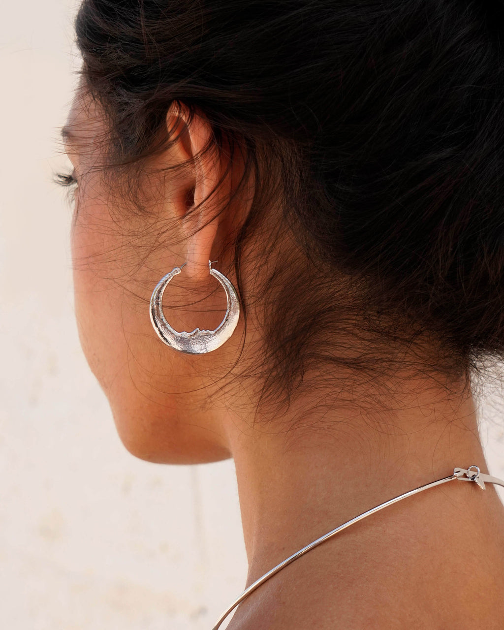 Luna earrings in silver featuring a crescent moon design with a subtle carved face on a woman's ear.